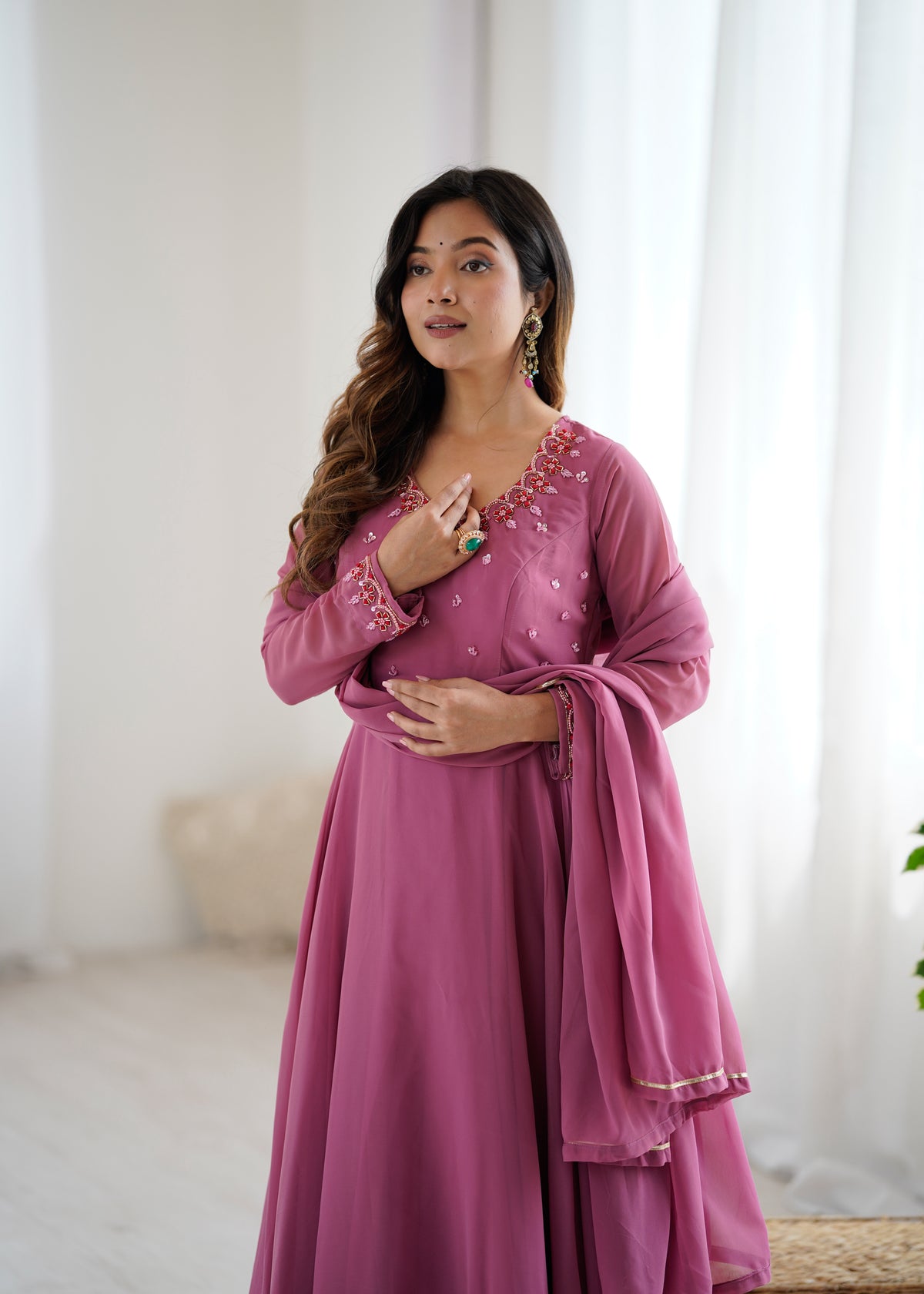 Woman wearing a pink traditional outfit with intricate detailing in a bright room.